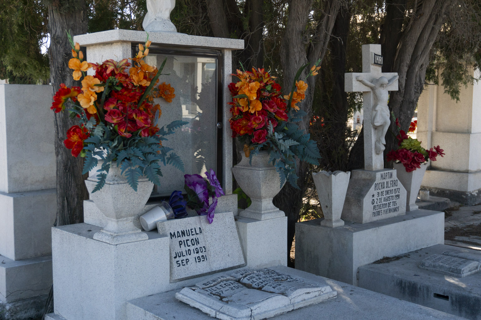 A grave marker with two matching boquets of flowers, a smaller one is tipped over